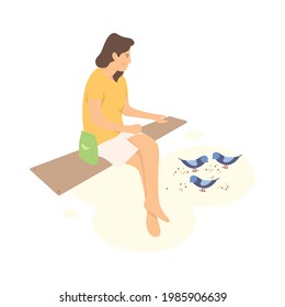 A woman sitting in the bench and feeding the birds.