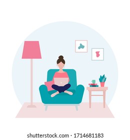 Woman sitting on an armchair with laptop  in her living room in period of self isolation and social distancing during Covid-19 virus epidemic. Stay at home concept. Freelance or studying concept.