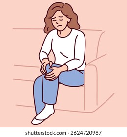 Woman sitting on couch holding knee in pain possibly due to joint inflammation or muscle strain