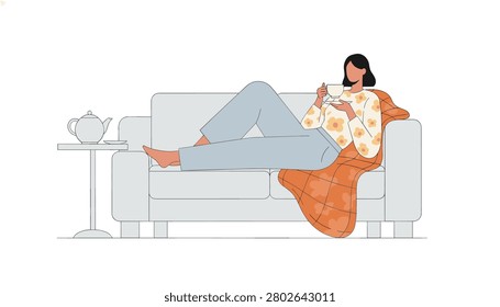 Woman sitting on sofa drinking tea with floral pattern top and orange blanket while using teapot on side table for cozy home leisure and relaxing afternoon.