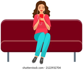 Woman sitting on sofa holds smartphone in her hand. Casual lady in headpones listening to music and browsing social media on mobile device. Girl on couch uses phone for chatting and surfing internet