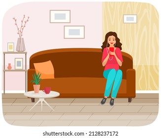 Woman sitting on sofa holds smartphone in her hand. Casual lady in headpones listening to music and browsing social media on mobile device. Girl on couch uses phone for chatting and surfing internet