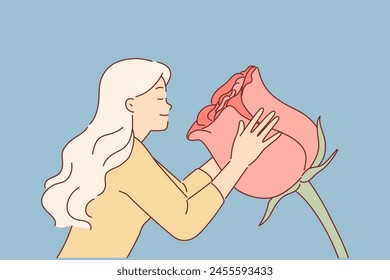 Woman sniffs huge rose flower, enjoying aroma of spring-blooming plant used to create perfume. Girl inhales smell of flower, wanting to have shampoo or body lotion made from rose petals