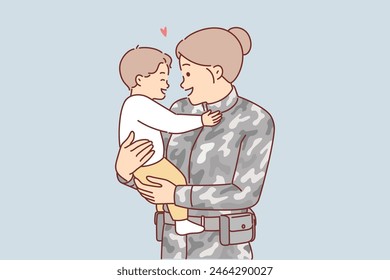 Woman soldier holds little son, who is rejoicing mother returns home after military service. Soldier girl in camouflage experiences maternal feelings and tenderness at sight of innocent child.