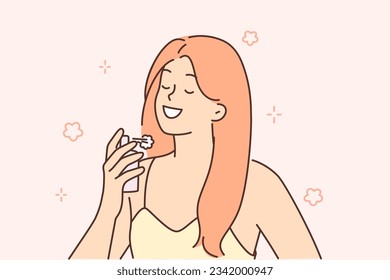 Woman sprinkles perfume on neck wanting to smell delicious at party or ceremonial event. Beautiful girl in evening dress holds bottle of perfume and smiles, demonstrating femininity and charm.