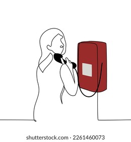 la mujer está parada frente a un teléfono en una cabina telefónica con un teléfono en la mano y se da vuelta mirando al espectador - un vector de dibujo de una línea. concepto para usar teléfono público de línea fija