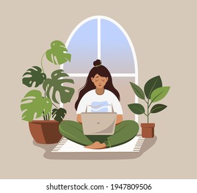 Woman stays at home and works at home with laptop sitting on floor near window.