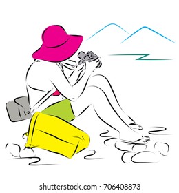 A woman stripped to the waist in a swimsuit and shorts is sitting on the rug with a camera in her hands. And looks at the mountains. On the head of a woman's hat from the sun. Woman with camera