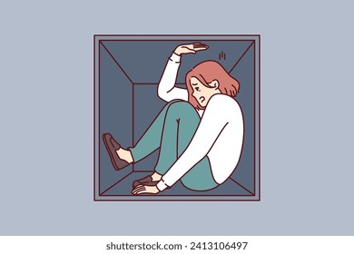 Woman suffering from claustrophobia sits in cramped box and feels pressure of walls, as metaphor for cramped housing. Girl experiences problems due to claustrophobia and fear of closed spaces.