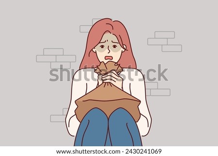 Woman suffering from panic attack holds paper bag for hyperventilation and restoration of normal psychological state. Girl sitting on floor near brick wall and experiencing stress due to panic attack