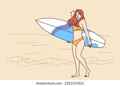 Woman surfer dressed in bikini walks along beach with surfboard and enjoys summer trip to tropical island. Surfer girl in bathing clothes smiles, walking on ocean and calls to go on trips and surf