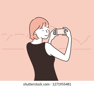 A woman is taking a landscape with her cell phone. hand drawn style vector design illustrations.