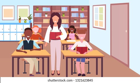 woman teacher reading book during lesson mix race pupils sitting desks education concept modern school classroom interior horizontal flat