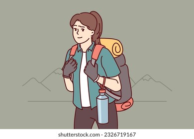 Woman tourist returns from hiking with large backpack on back and bottle of water posing near mountains. Girl is fond of hiking and loves to travel to natural parks and national reserves