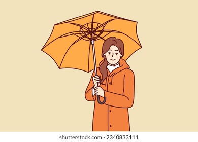 Woman with umbrella is dressed in oilcloth coat so as not to get wet from rain on autumn walk. Happy girl holding umbrella and looking at screen offering to take walk during rainy weather