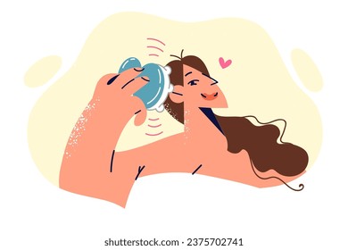 Woman uses head massager after getting out of shower to relieve cranial pressure and stress. Girl wrapped in towel holds electronic body massager and enjoys vibration effects of gadget.