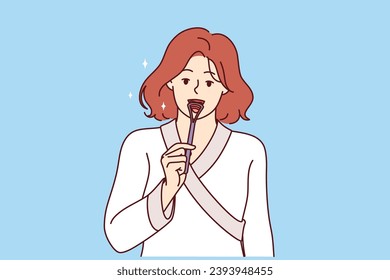 Woman uses tongue brush to clean mouth from germs, showing example of hygiene education. Girl in bathrobe brushes tongue to improve health and preventively combat formation of caries