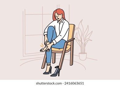 Woman with varicose veins feels pain in legs due to uncomfortable high-heeled shoes, sits on chair in apartment. Girl needs medicinal ointment to cure varicose veins or calluses on heel