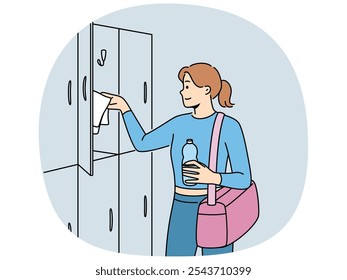 Woman visitor to gym stands near lockers for personal belongings and prepares for sports workout. Girl with bag for sportswear and bottle of water visits gym to maintain good figure