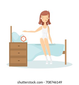 Woman waking up. Young sleepy woman sits on bed switching off alarm clock.