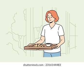 Woman wants to have breakfast in garden or in backyard of own house carries tray of hot tea and croissants. Happy girl carries delicious breakfast on tray to satisfy hunger before hard day at work.