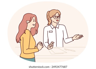Woman working at reception in hotel or beauty salon consults client, helps to choose beautician and best procedure. Girl visiting cosmetology clinic stands near reception with administrator