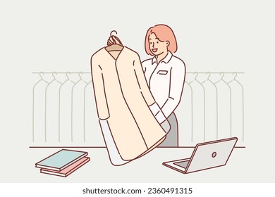 Woman works at dry cleaning and stands behind counter with client clean coat, next to rack of clothes waiting to be professionally laundered. Girl dry cleaning manager passes jacket to customer