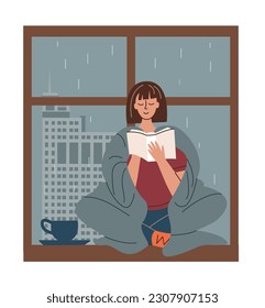 Woman wrapped in cozy blanket reads book sittig on windowsill. It's raining outside window.