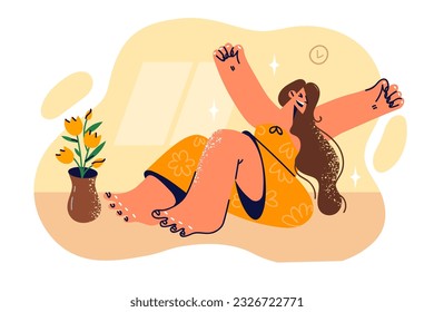 Woman yawns sitting on floor in apartment, stretching arms to sides after waking up early and rejoicing at weekend with opportunity to relax. Girl yawns or does morning wellness exercises
