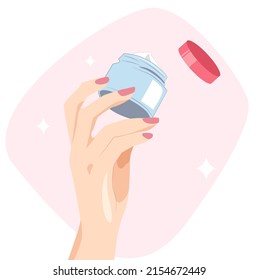 A woman's hand with a pink manicure holds a blue jar of cream in her hands. Beauty cosmetics for face and body care. Moisturizing anti-wrinkle cream