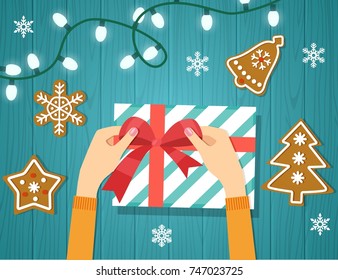  Woman's hands give wrapped christmas holiday handmade present in paper with red ribbon. Gingerbread cookie. Wooden board. Banners. Flat vector illustration.