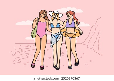 Women in bikinis walk along beach on seashore, enjoying summer holiday at hot resort. Three tourist girls pose on sandy beach, inviting you to visit tropical island to sunbathe and swim