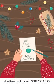 Women's hands with pen write Christmas card on dark wooden table. Winter festive vertical background. Preparation for holidays concept. Top view flat design illustration