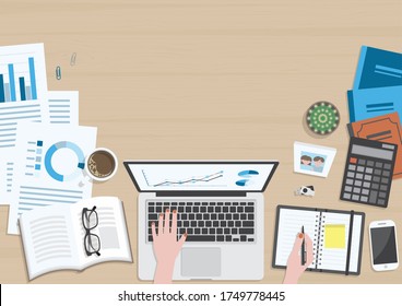 Wood textured desk from top view with hands of woman working on laptop computer and writing on organizer with office supplies, coffee mug, photo frame, books and document