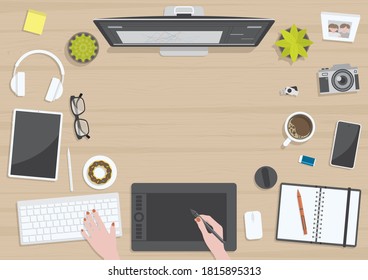 Wood textured table from top view with hands of woman drawing on digital graphic tablet with monitor, camera, tablet, headphones and gadgets, design for work from home concept