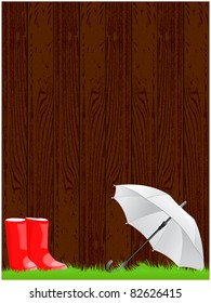 Wooden background with green grass, red rubber boots and open white umbrella