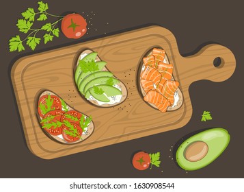 Wooden cooking board with bruschetta or sandwiches with curd cheese, avocado, tomatoes and red fish. Seasoning with fresh herbs, parsley or arugula.