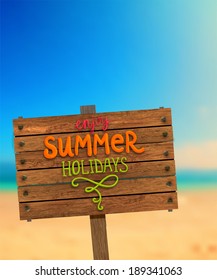 Wooden Plaque with "Enjoy Summer Holidays" Lettering. Blurred Background. Summer Beach. Sand and Ocean. Blue Sky.