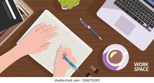 A workspace with a person writing and there are books, laptops, ornamental plants and coffee cups on a wooden table