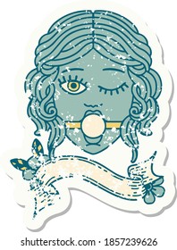 worn old sticker with banner of a winking female face wearing ball gag