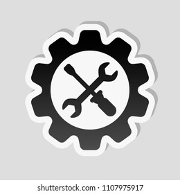 Wrench and screwdriver in gear. Sticker style with white border and simple shadow on gray background