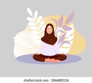 Yoga meditation at home. Muslim woman is meditating in lotus position. A young woman in a hijab practices yoga on a background of plant leaves. Relaxing while enjoying your vacation. 