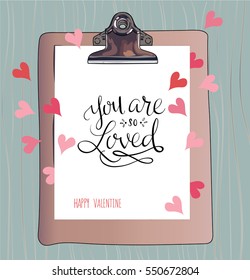 You are so loved is an illustration of a clipboard with a message of valentines day with blue background, ornaments, hearts and handmade lettering.