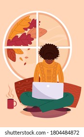 A young African woman working on laptop from home. Freelance by window in the autumn.
