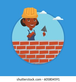 Young african-american bricklayer in uniform and hard hat. Smiling bicklayer working with spatula and brick on construction site. Vector flat design illustration in the circle isolated on background.