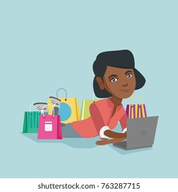 Young african-american woman using a laptop for online shopping. Woman lying with a laptop and shopping bags around her. Woman doing online shopping. Vector cartoon illustration. Square layout.