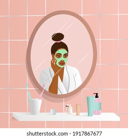 Young afroamerican woman do her beauty routine. Woman looking in mirror and apply face mask in bathroom. Mirror reflection of skin care.