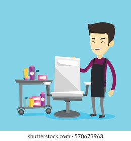 Young asian male barber standing near armchair and table with cosmetics in barber shop. Professional male barber standing at workplace in barber shop. Vector flat design illustration. Square layout.