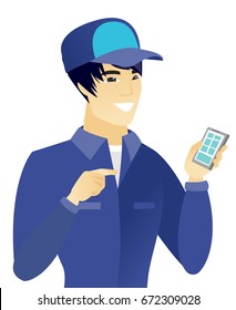 Young asian mechanic holding mobile phone and pointing at it. Smiling happy mechanic using a mobile phone. Vector flat design illustration isolated on white background.