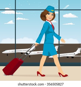 young attractive stewardess with luggage walking through airport terminal 